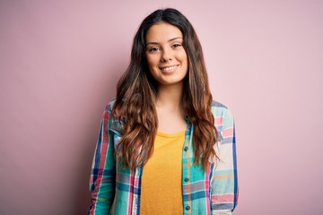 Young beautiful brunette woman wearing casual colorful shirt standing over pink background with a happy and cool smile on face. Lucky person.