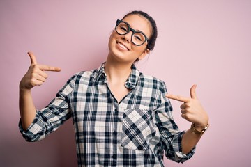 Young beautiful brunette woman wearing casual shirt and glasses over pink background looking...