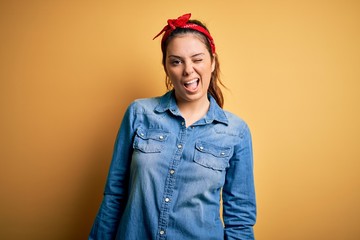 Young beautiful brunette woman wearing casual denim shirt and hair handkerchief winking looking at the camera with sexy expression, cheerful and happy face.