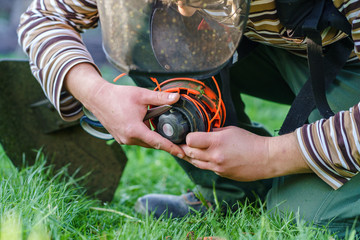 Close up on string trimmer head unknown caucasian man holding and repairing weed cutter replacing...