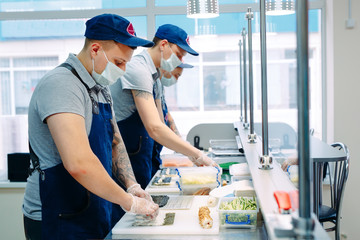 Obraz premium Sushi delivery. Masked and gloved chefs prepare sushi In the Restaurant's kitchen.