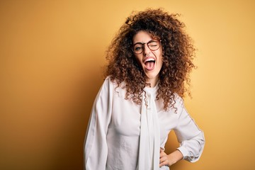 Young beautiful brunette woman with curly hair and piercing wearing shirt and glasses winking...
