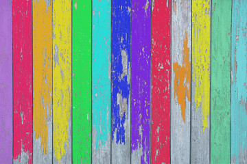 Bright wooden fence painted in rainbow color with peeling paint