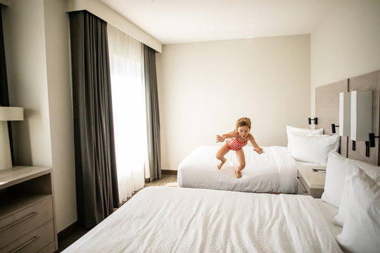 A young girl having fun and jumping on the bed in a hotel room.