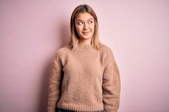 Young beautiful blonde woman wearing winter wool sweater over pink isolated background smiling looking to the side and staring away thinking.