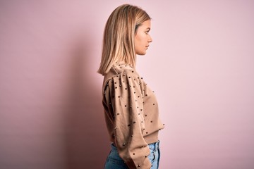 Young beautiful blonde woman wearing fashion sweater over pink isolated background looking to side,...