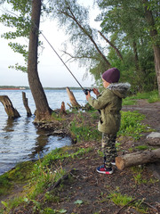The child holds spinning in his hands and spins the coil pulling out a catch. The concept of training a child fishing. The concept of relaxation by the water, river, lake.