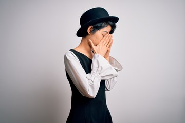 Young beautiful asian girl wearing casual dress and hat standing over isolated white background with sad expression covering face with hands while crying. Depression concept.