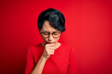 Young beautiful asian girl wearing casual t-shirt and glasses over isolated red background feeling unwell and coughing as symptom for cold or bronchitis. Health care concept.