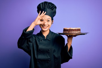 Young chinese chef woman wearing cooker uniform and hat holding tray with cake with happy face...