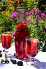 Still life with homemade fruit lemonade in a bottle and glasses on a table in the open air a background of flowers. Closeup