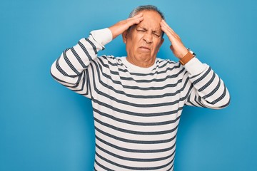 Senior handsome grey-haired man wearing striped sweater over isolated blue background suffering from headache desperate and stressed because pain and migraine. Hands on head.