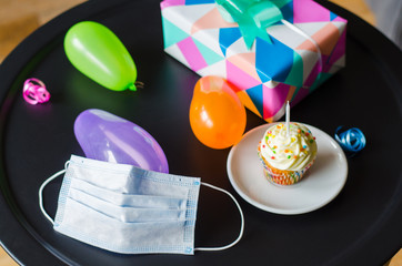 Quarantine birthday in isolation. Social distance. Birthday cupcake, face mask, gifts and holiday accessories.