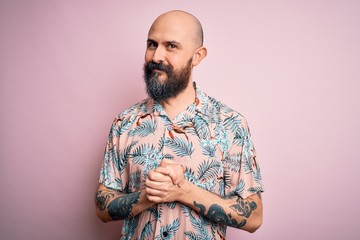 Handsome bald man with beard and tattoo wearing casual floral shirt over pink background with hands together and crossed fingers smiling relaxed and cheerful. Success and optimistic