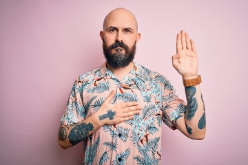 Handsome bald man with beard and tattoo wearing casual floral shirt over pink background Swearing with hand on chest and open palm, making a loyalty promise oath