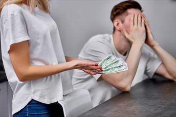 wife outraged why husband brings so little money in a family wallet, she expresses dissatisfaction with husband's working capacity, man close face with hands