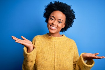 Young beautiful African American afro woman with curly hair wearing yellow casual sweater smiling showing both hands open palms, presenting and advertising comparison and balance