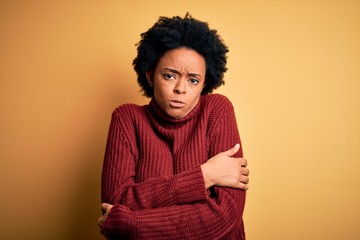 Fototapeta na wymiar Young beautiful African American afro woman with curly hair wearing casual turtleneck sweater shaking and freezing for winter cold with sad and shock expression on face