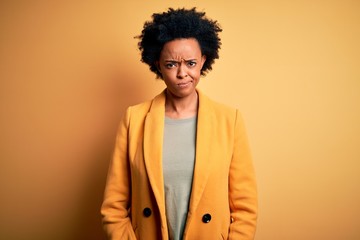 Young beautiful African American afro businesswoman with curly hair wearing yellow jacket skeptic...