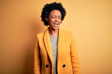 Fototapeta na wymiar Young beautiful African American afro businesswoman with curly hair wearing yellow jacket winking looking at the camera with sexy expression, cheerful and happy face.