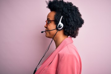 Young African American call center operator woman with curly hair using headset looking to side,...