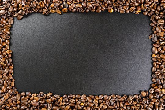 Background made of fresh roasted coffee beans lying flat on a black background with copy space in the shape of a rectangle. © Michal