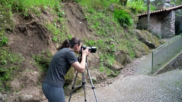A young girl, a photographer, in a forest area, takes pictures of an old house and beautiful nature.