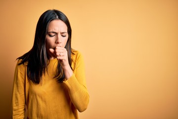 Young brunette woman with blue eyes wearing casual sweater over yellow background feeling unwell...