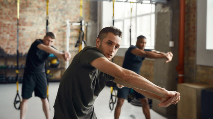 Fototapeta na wymiar Make yourself stronger than your excuses. Portrait of diverse athletic men stretching body while working out together in industrial gym. Group training concept