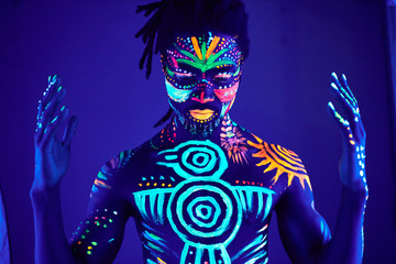 portrait of african man painted in fluorescent paint on face and muscular torso, studio shot with...