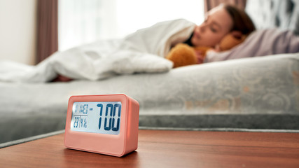 Get up early. Asleep caucasian young woman in the background with digital alarm clock in focus