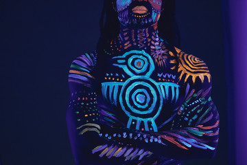 handsome young african guy has unusual cosmic prints on naked body and face. fashionable design prints glowing on neon light