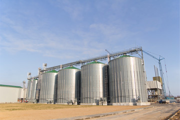 Construction of a feed mill agro-processing plant for processing and silos for drying cleaning and storage of agricultural products, flour, cereals and grain.  Silver tanks view from afar.