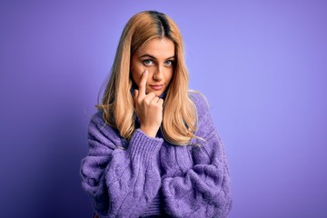 Young beautiful blonde woman wearing casual turtleneck sweater over purple background Pointing to the eye watching you gesture, suspicious expression