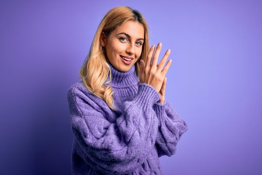 Young beautiful blonde woman wearing casual turtleneck sweater over purple background clapping and applauding happy and joyful, smiling proud hands together