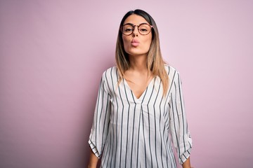 Young beautiful woman wearing casual striped t-shirt and glasses over pink background looking at the camera blowing a kiss on air being lovely and sexy. Love expression.