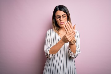 Young beautiful woman wearing casual striped t-shirt and glasses over pink background Suffering pain on hands and fingers, arthritis inflammation