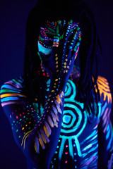 handsome african guy with UV body art close his face, colorful fantastic prints glows in darkness