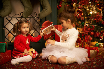 Little sisters unpack gifts smile laugh Cozy atmosphere of Christmas New Year Christmas tree...