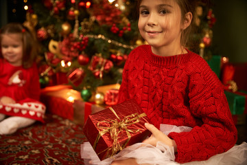 Little sisters unpack gifts smile laugh Cozy atmosphere of Christmas New Year Christmas tree garlands and a fireplace Dreams come true Children Baby
