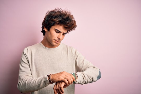 Young handsome man wearing casual t-shirt standing over isolated pink background Checking the time on wrist watch, relaxed and confident