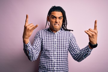 Young handsome african american afro man with dreadlocks wearing casual shirt shouting with crazy expression doing rock symbol with hands up. Music star. Heavy music concept.