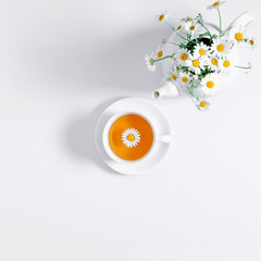 White chamomiles and teapot on white background. Herbal tea of chamomile flower. Chamomile tea...