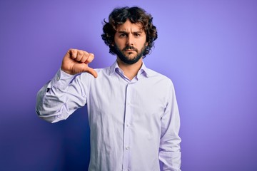 Fototapeta premium Young handsome business man with beard wearing shirt standing over purple background looking unhappy and angry showing rejection and negative with thumbs down gesture. Bad expression.