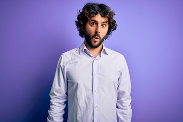 Young handsome business man with beard wearing shirt standing over purple background In shock face, looking skeptical and sarcastic, surprised with open mouth