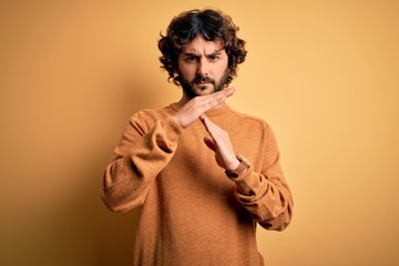 Young handsome man with beard wearing casual sweater standing over yellow background Doing time out...