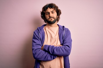 Young handsome sporty man with beard wearing casual sweatshirt over pink background skeptic and nervous, disapproving expression on face with crossed arms. Negative person.