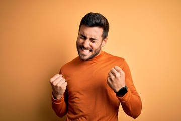 Young handsome man with beard wearing casual sweater standing over yellow background very happy and...