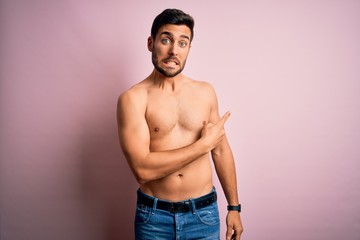 Young handsome strong man with beard shirtless standing over isolated pink background Pointing...