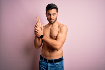 Young handsome strong man with beard shirtless standing over isolated pink background Holding...